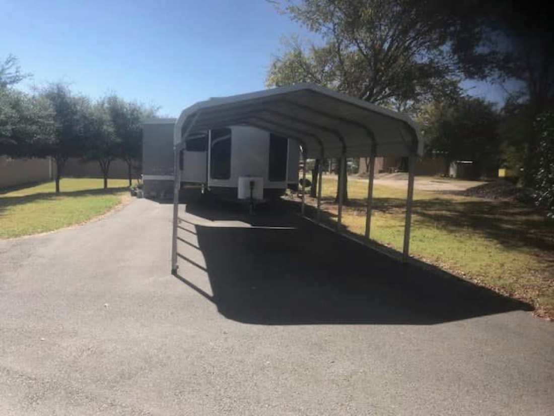 Fifth-wheel RV parked under a covered carport site with a long paved driveway at ABC RV Park